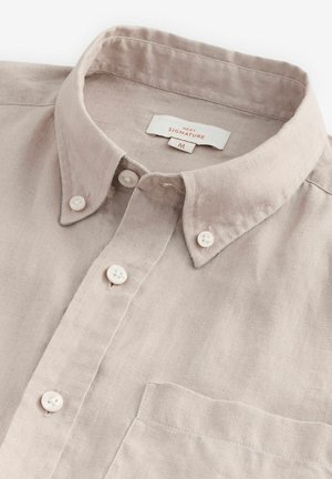 Lyse beige linned skjorte med knap-krave, udstyret med hvide knapper, en brystlomme og et mærke med teksten "NEXT SIGNATURE M."
