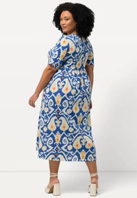 Sininen puolipitkä mekko, jossa on oranssi ja valkoinen kukkakuosi, lyhyet hihat, vyötäröllä vyö ja löysä siluetti.