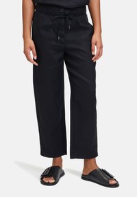 Pantalons culotte en lin noir avec une taille à cordon, fermeture à bouton et jambes larges. Associés à des sandales à glissière noires avec un accent décoratif.