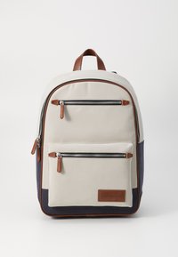 Zaino con corpo in tela crema, fondo blu navy, dettagli in pelle, due tasche anteriori con zip e una maniglia superiore per il trasporto.