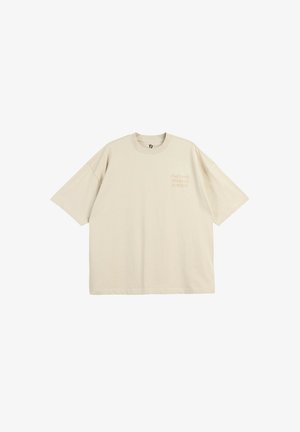 Beżowy, oversize t-shirt z krótkim rękawem, okrągłym dekoltem i małym napisem "That Level SPARKLE EDITION" na lewej piersi.