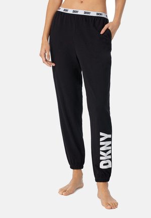 Jogging en coton noir avec un logo DKNY blanc sur la jambe gauche. Caractéristiques d'une taille élastique et de poches, se rétrécissant au niveau de la cheville.