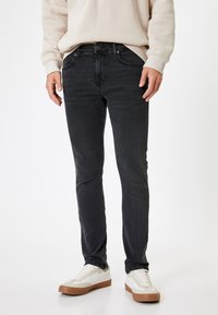Jeans negros slim-fit hechos de denim con una textura suave. Presentan bolsillos frontales, cierre de botón y están combinados con zapatillas blancas.