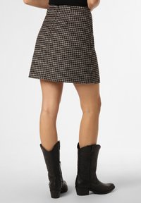 Une mini-jupe évasée à motif pied-de-poule noire et crème, associée à de grandes bottes de cowboy noires avec des motifs embossés.