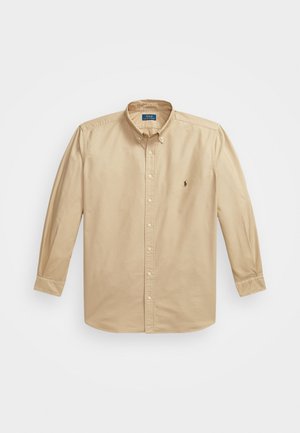 Béžová košeľa s dlhým rukávom a gombíkovým zapínaním vyrobená z bavlny. Má klasický golier, zapínanie na gombíky a malé logo na ľavej strane hrudníka.