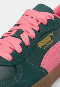 Green suede sneaker with a pink lace-up design, featuring a gold Puma logo on the side. The sole is brown and textured.