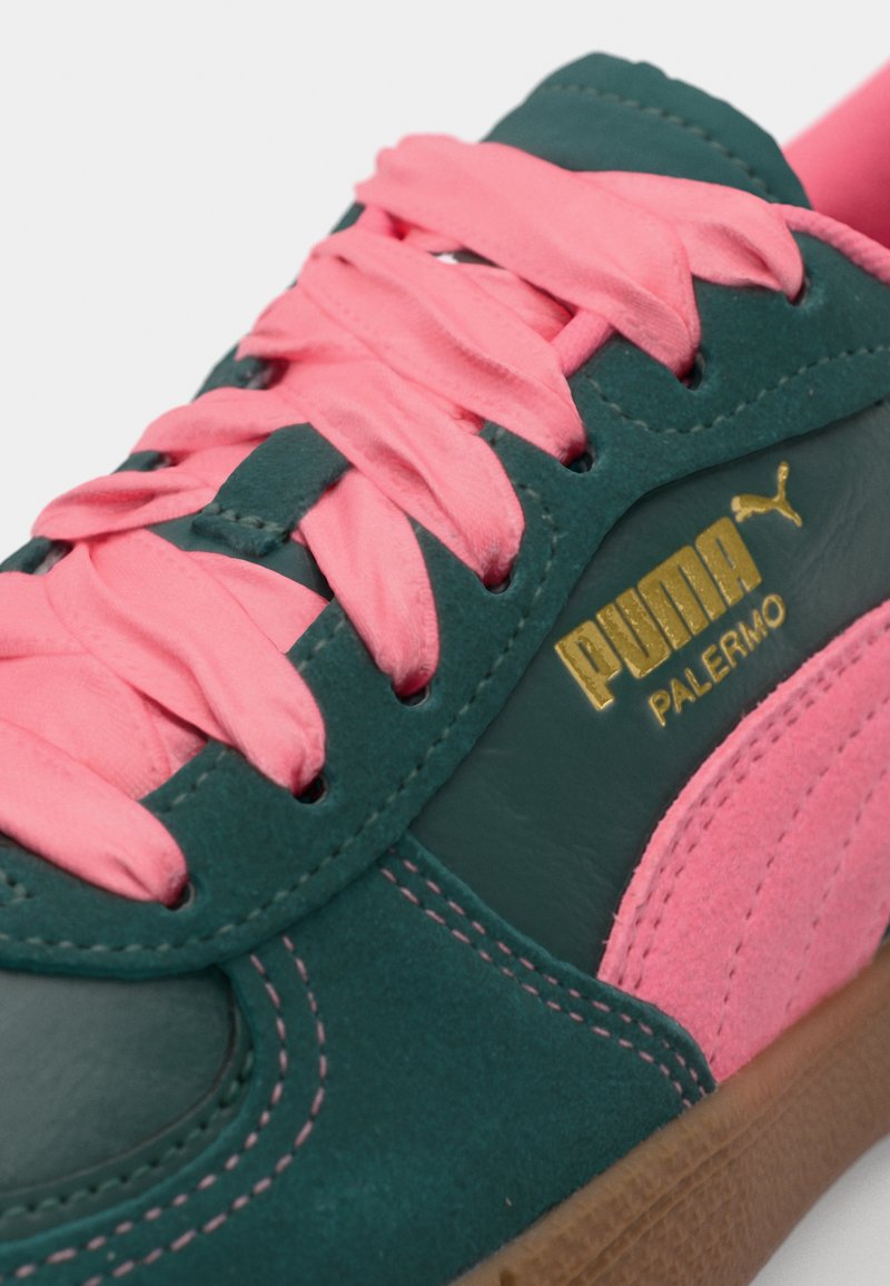 Zapatilla de ante verde con un diseño de cordones rosa, que presenta un logo dorado de Puma en el lateral. La suela es marrón y texturizada.