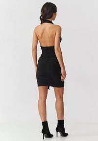Czarna sukienka na halter z marszczeniem, dopasowany krój i otwarty tył. Połączona z czarnymi kozakami na obcasie do kostki.