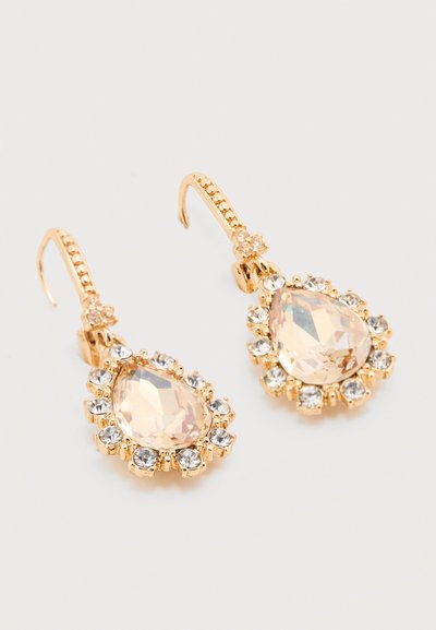 Χρυσά σκουλαρίκια με γάντζο, με μεγάλο δάκρυ σχήματος διαφανές πολύτιμο λίθο, περιβαλλόμενο από μικρότερους στρογγυλούς διαφανείς λίθους, πάνω σε ουδέτερο φόντο.
