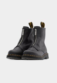 Μαύρα δερμάτινα μποτάκια μέχρι τον αστράγαλο με φερμουάρ μπροστά, κίτρινη ραφή και λουράκια τράβηγματος σε βρόχο. Ανθεκτικές σόλες με υφή.