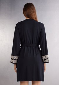 Zwarte jurk met lange mouwen, voorzien van kantaccenten bij de manchetten. Gemaakt van zachte stof met een ceintuur in de taille voor een relaxte pasvorm.