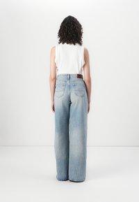 Jeans de mezclilla de pierna ancha en azul claro con un acabado desgastado, cinco bolsillos y un parche de cuero marrón en la cinturilla trasera.