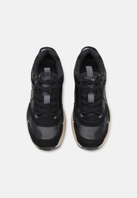 Baskets noires avec un mélange de daim et de mesh, présentant des accents gris, des lacets ronds et une semelle en caoutchouc de couleur claire.