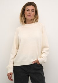 Light beige knit sweater with a round neckline, raglan sleeves, and ribbed hem and cuffs. The texture appears soft and cozy.