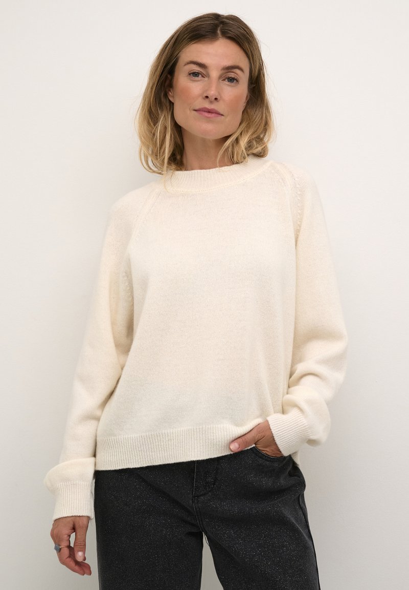 Light beige knit sweater with a round neckline, raglan sleeves, and ribbed hem and cuffs. The texture appears soft and cozy.