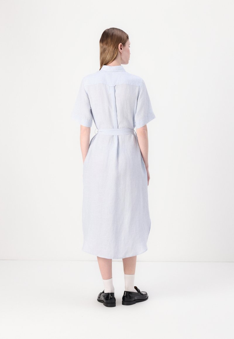 Himmelblaues Leinenkleid mit kurzen Ärmeln, einem Hemdkragen, taillierter Taille und knielangem Saum. getragen mit schwarzen Schuhen und weißen Socken.