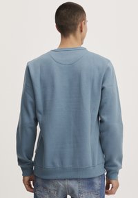 Blauwe katoen sweatshirt met lange mouwen, ronde hals, ribbenmanchetten en -zoom, en een relaxte pasvorm. Gladde textuur, minimale details.