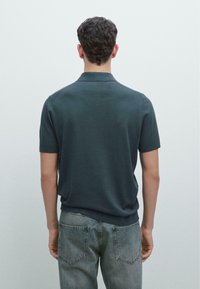 Ciemnozielona koszulka polo z krótkim rękawem, z żebrowanym kołnierzem, gładką teksturą i dopasowanym fasonem, zestawiona z jasnoszarymi dżinsami.