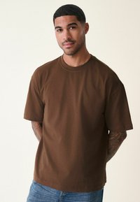 Brun bomulds T-shirt med rund hals, korte ærmer og en afslappet pasform. Har en glat tekstur og et minimalistisk design.