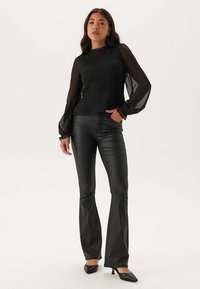 Blusa nera con corpino strutturato e maniche trasparenti abbinata a pantaloni neri attillati a gamba ampia e tacchi a punta neri. Design semplice ed elegante.