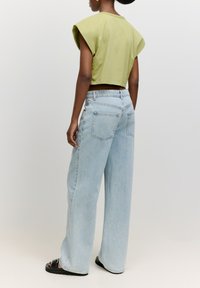 Korte groene top met capmouwen en detail in de achternaad, gecombineerd met lichtblauwe wide-leg jeans met twee achterzakken en een vervaagde wassing.