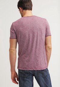 Lyhythihainen t-paita heather-burgundin värisestä kankaasta, jossa on pyöreä pääntie. Ominaisuuksiin kuuluu rento malli ja siisti ompelu, yhdistettynä tummansinisiin farkkuihin.