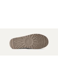 Suela de goma marrón con un patrón de textura en relieve, que presenta un logo circular central y líneas radiales para mejorar el agarre y la tracción.