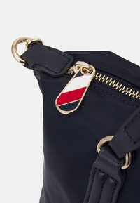 Tirette de fermeture éclair de sac marine avec des rayures diagonales rouges, blanches et noires et anneau en métal doré et accessoires sur tissu foncé.