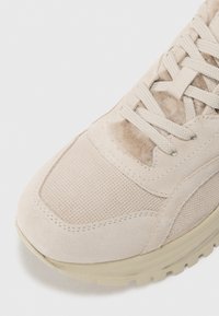 Baskets de sport beige avec une tige en maille texturée et en suede, bout rond et fermeture à lacets plates. Semelle en caoutchouc légèrement surélevée avec un motif de grip.