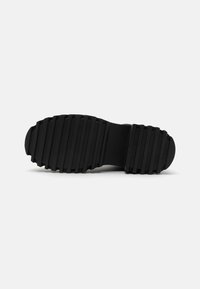 Suela de zapato de goma negra con prominentes ranuras horizontales para tracción, punta redondeada y una construcción sólida para durabilidad.