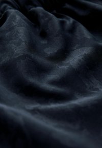 Tessuto nero con una texture morbida e liscia e leggere variazioni di lucentezza. Presenta sottili motivi tonali e cade fluidamente.