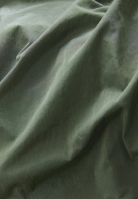 Ciemnooliwkowy materiał z delikatnym połyskiem, z miękkimi zmarszczkami i gładką fakturą. Materiał delikatnie opada, podkreślając swoją giętkość.