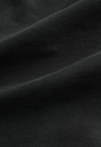 Schwarzer Stoff mit glatter Textur, der ein dezentes geripptes Muster aufweist. Gefaltet, wobei das Licht sanft reflektiert und weiche Schatten erzeugt.