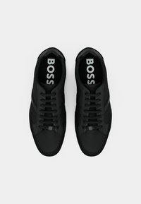 Baskets noires avec une tige en tissu lisse, bout rond, lacets plats et logo sur la semelle intérieure. Design simple avec des accents minimalistes.