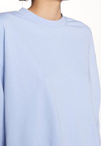 Felpa oversized blu chiaro con colletto rotondo. Il tessuto appare morbido e liscio, con una vestibilità rilassata e casual.