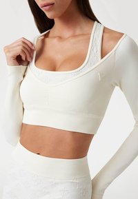 Top sportivo bianco a coste con maniche lunghe, scollo ampio e design testurizzato. Presenta un effetto a strati con una silhouette aderente.