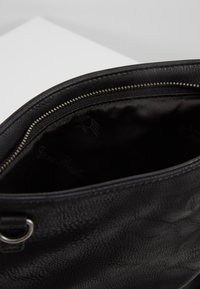 Borsa a tracolla in pelle nera con superficie testurizzata, chiusura con cerniera e fodera interna liscia nera con dettagli di marchio delicati.