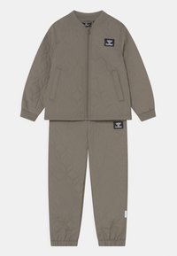 Dwuczęściowy komplet w kolorze taupe, pikowany, z kurtką na zamek i spodnie z elastycznymi mankietami, ozdobiony naszywkami z logo hummel na piersi i udzie.