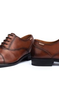 Scarpe eleganti in pelle marrone con finitura liscia, punta tonda e lacci piatti. Presentano una cucitura delicata e un tacco basso in gomma nera.