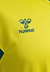 Gul sportströja med en blå Hummel-logga, tillverkad av polyester, med en mjuk textur och kontrasterande blå detaljer vid halsringningen.