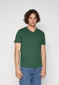 Green v-neck t-shirt made of soft fabric, featuring short sleeves and a comfortable fit. Worn with blue denim jeans.
