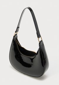 Sac à main brillant en forme de croissant noir avec une courte bandoulière et une fermeture éclair dorée visible sur un fond blanc.