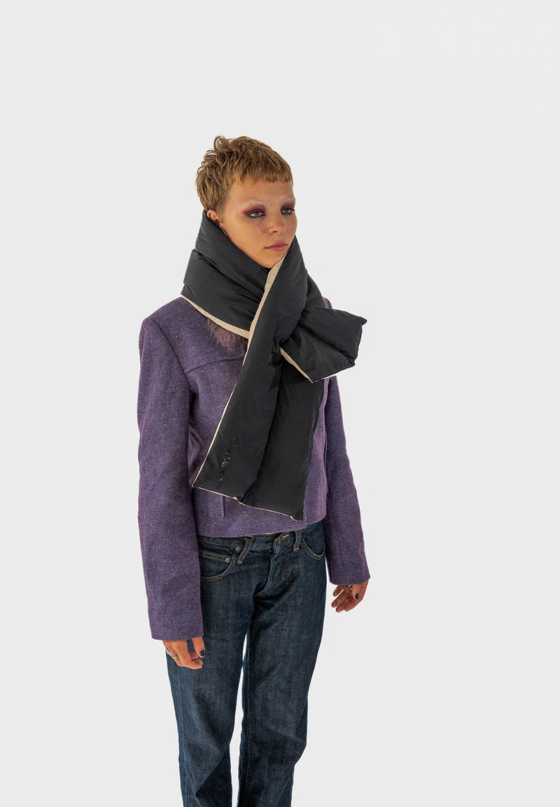 Sort tørklæde med cremefarvet kant, båret om halsen, parret med en struktureret lilla jakke og mørk denimjeans. Tørklædet har en glat overflade.