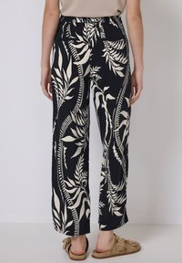 Black wide-leg pants featuring a bold cream leaf pattern, made of lightweight fabric, with an elastic waistband and side pockets.