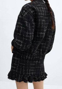 Zwart tweed jasje en mini-jurk set met een gestructureerde stof, wit ruitpatroon en een gekrulde zoom op de jurk.