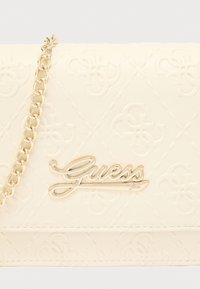 Τσάντα Guess χρώματος κρέμα με ανάγλυφο μοτίβο λογότυπου, λουράκι από χρυσή αλυσίδα και μεταλλική διακόσμηση λογότυπου σε στυλ  γραφής. Λείος υφή.