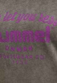 Šedá látka s výrazným fialovým textem "hummel" a "SPORTSWEAR CO. 1923", která vykazuje mírně zandranou texturu.