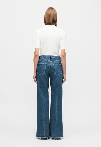 Λευκό ριμπ κοντομάνικο τοπ με ψηλό λαιμό, σε συνδυασμό με φαρδιά μπλε τζιν παντελόνια με σκισμένες άκρες και πίσω τσέπες.