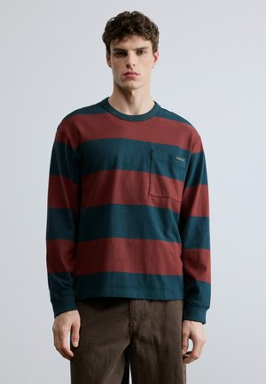 Hosszú ujjú ing, piros és türkiz vízszintes csíkokkal, kerek nyakkivágással és bal oldali mellzsebbel. Pamut anyagból készült.