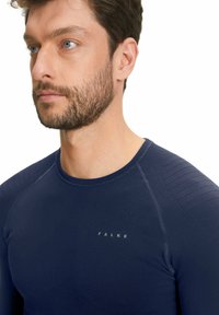 Navyblauw langemouwen shirt met gestructureerde schouderpanelen, ronde halslijn en subtiele 'FALKE' logo op de borst. Vloeiende stofafwerking.